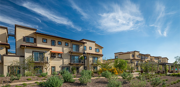 Sizable landscaped area in front of three-story beige stucco apartment building.